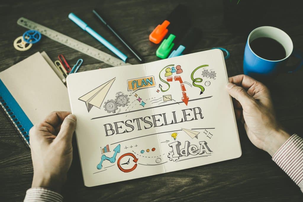 Complete self-publishing coaching: Someone holds a notebook with a "Bestseller Plan" and ideas, surrounded by materials on a desk.